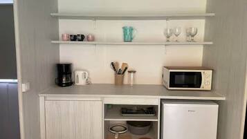 Een kleine keuken met een magnetron, koffiezetapparaat en opbergkasten.