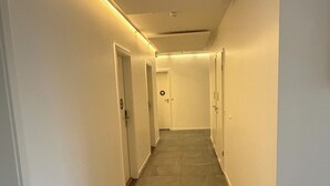 Un pasillo con suelo de baldosas, paredes blancas y puertas a ambos lados.