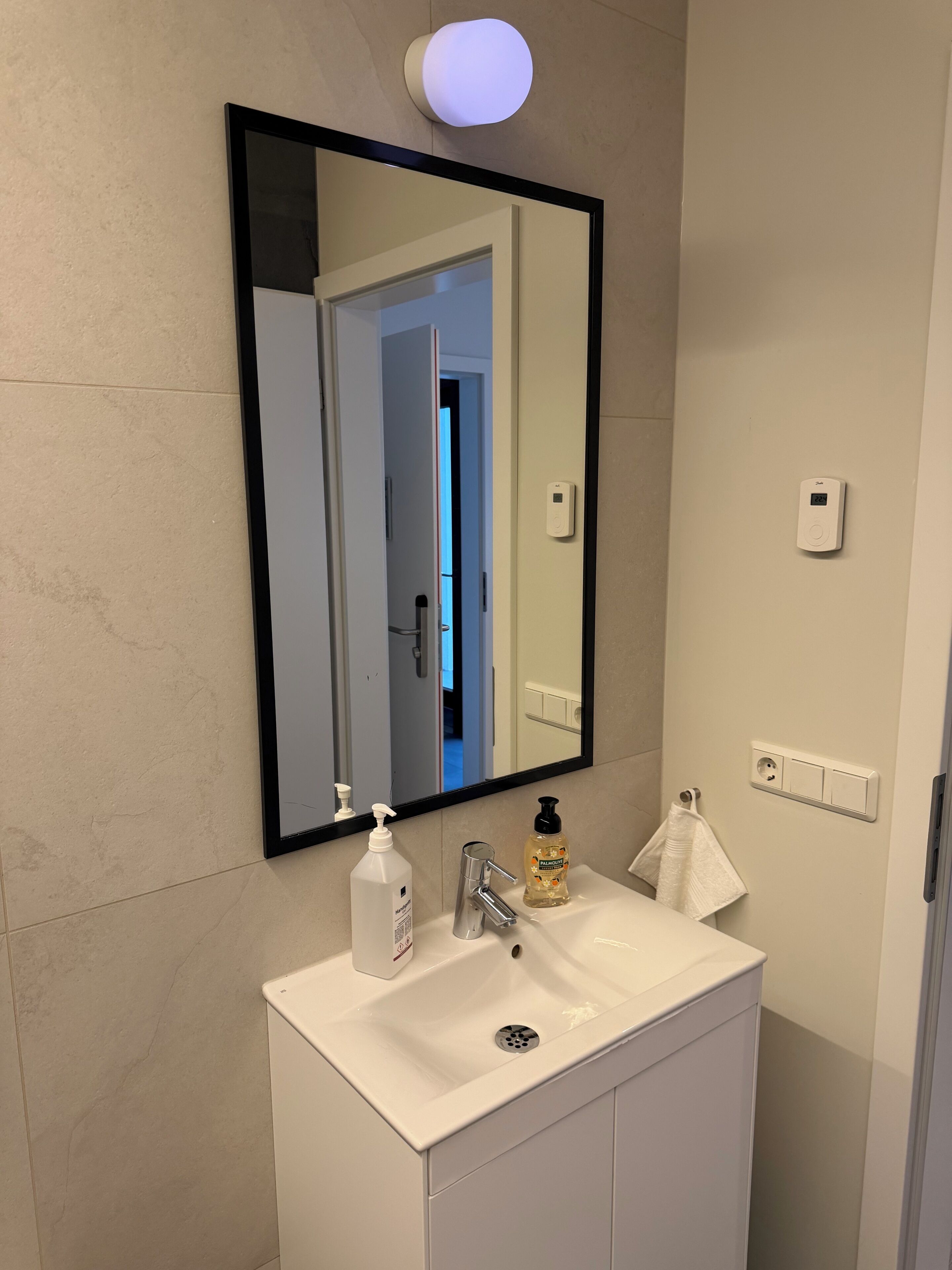 A bathroom with a white sink, a mirror, a hand soap dispenser, a bottle of liquid soap, and a towel.