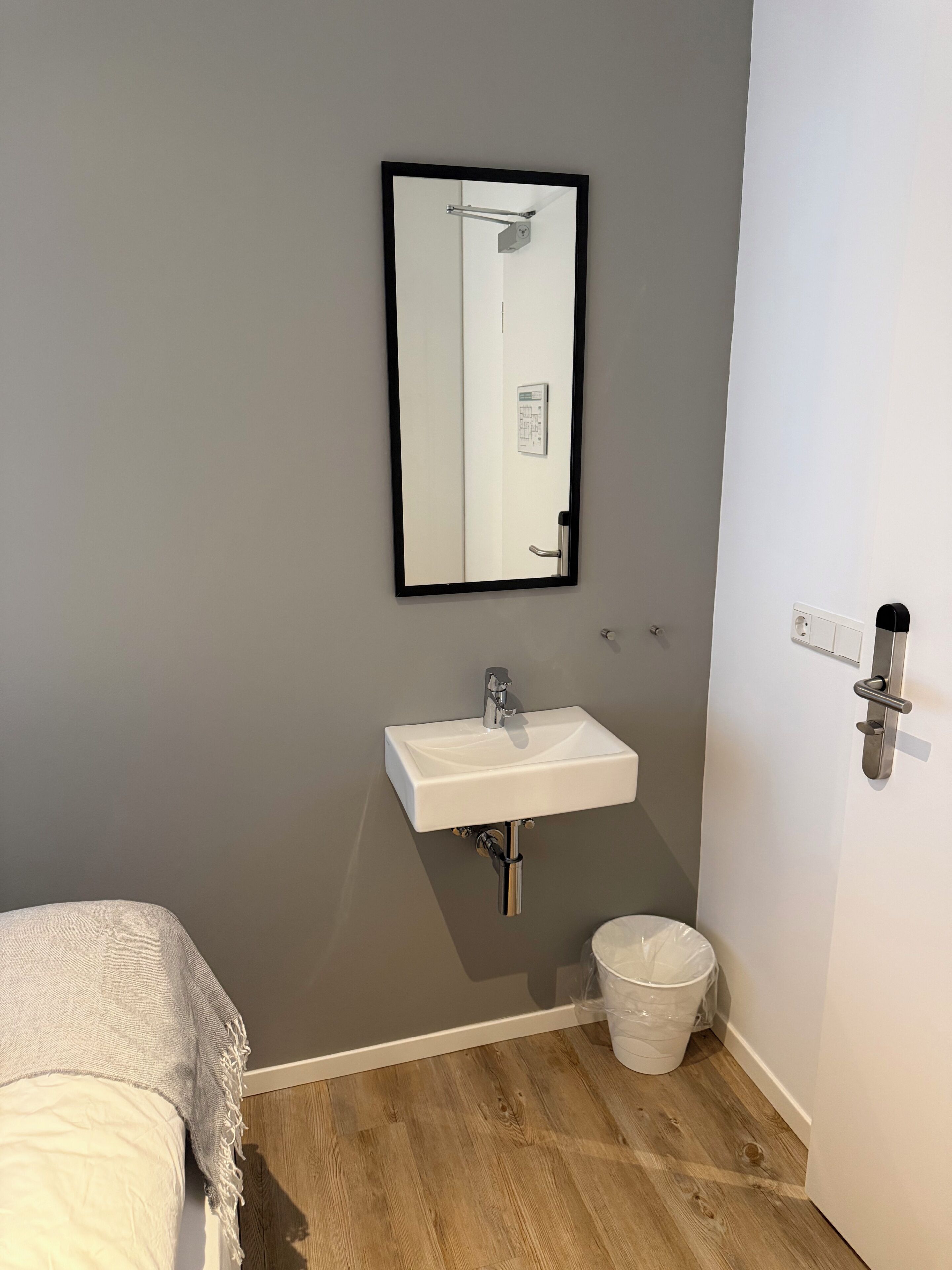 Une petite salle de bain avec un lavabo blanc, un miroir, une serviette et une poubelle.