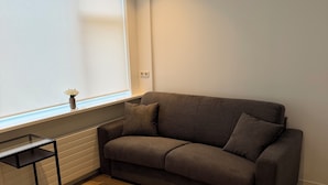 Una habitación con un sofá marrón, una mesita y una ventana con persianas.