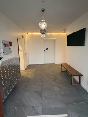 A hotel lobby with a bench, a door with a number, a coat rack, and a ceiling light fixture.