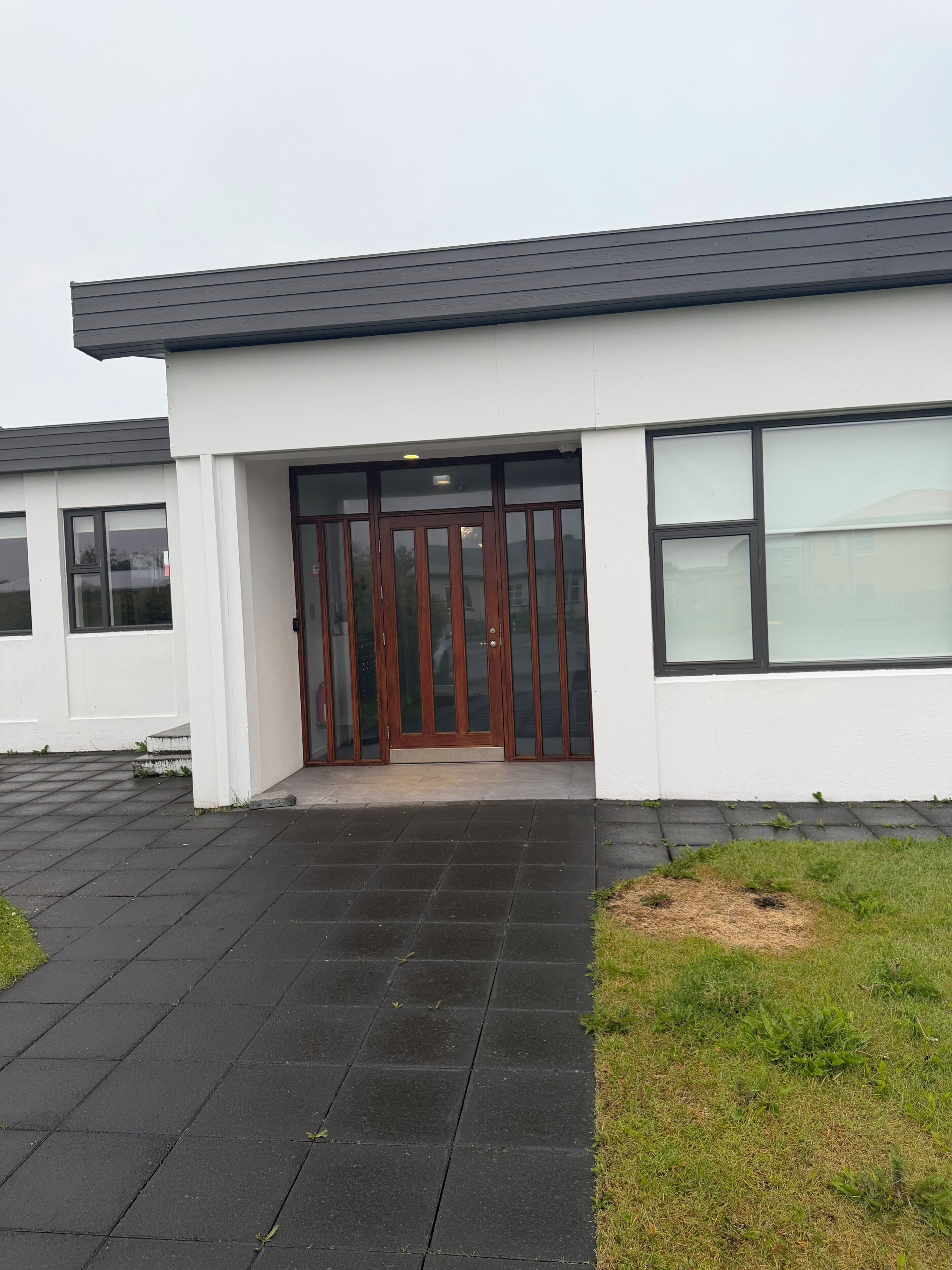 A modern building with a flat roof, large windows, and a central entrance with a glass door.