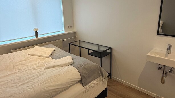Un dormitorio con cama, mesita de noche y baño con lavabo y espejo.