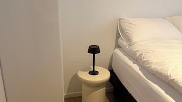 Un dormitori petit i ben organitzat amb un llit individual, una taula de nit amb una làmpada i un terra de fusta.