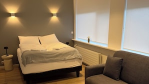 Un dormitorio con una cama, un sofá gris, suelo de madera y luces fijadas a la pared.