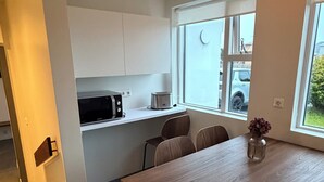 Una cocina moderna con armarios blancos, microondas y tostadora. Hay una mesa de comedor con sillas y un florero con flores.