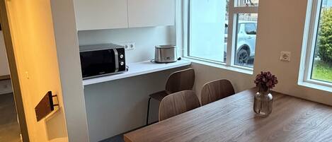 A modern kitchen with white cabinets, a microwave, and a toaster. There is a dining table with chairs and a vase with flowers.