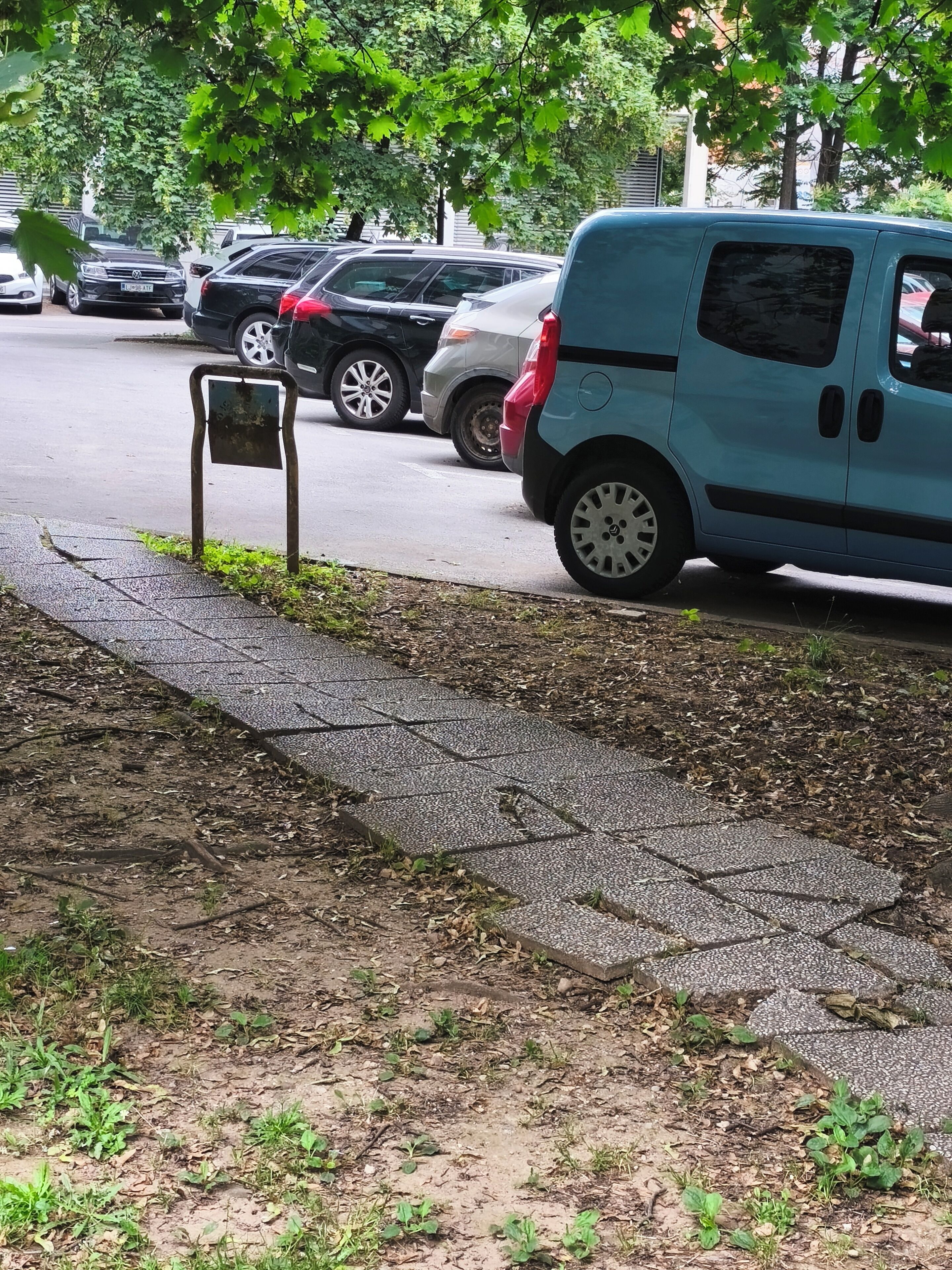 A parking area with a blue van, a metal sign, and a paved walkway.