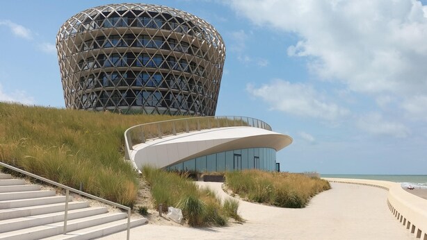 Ein modernes Gebäude mit einem einzigartigen, kugelförmigen Design, einem gewundenen Weg davor und einem Strand im Hintergrund.
