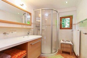 A bathroom with a shower, a sink, a mirror, and a window.