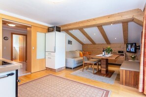A compact room with a kitchenette, a sofa, a dining table, and a TV.