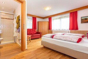 A bedroom with a bed, a red sofa, a wooden wardrobe, and a shower area.