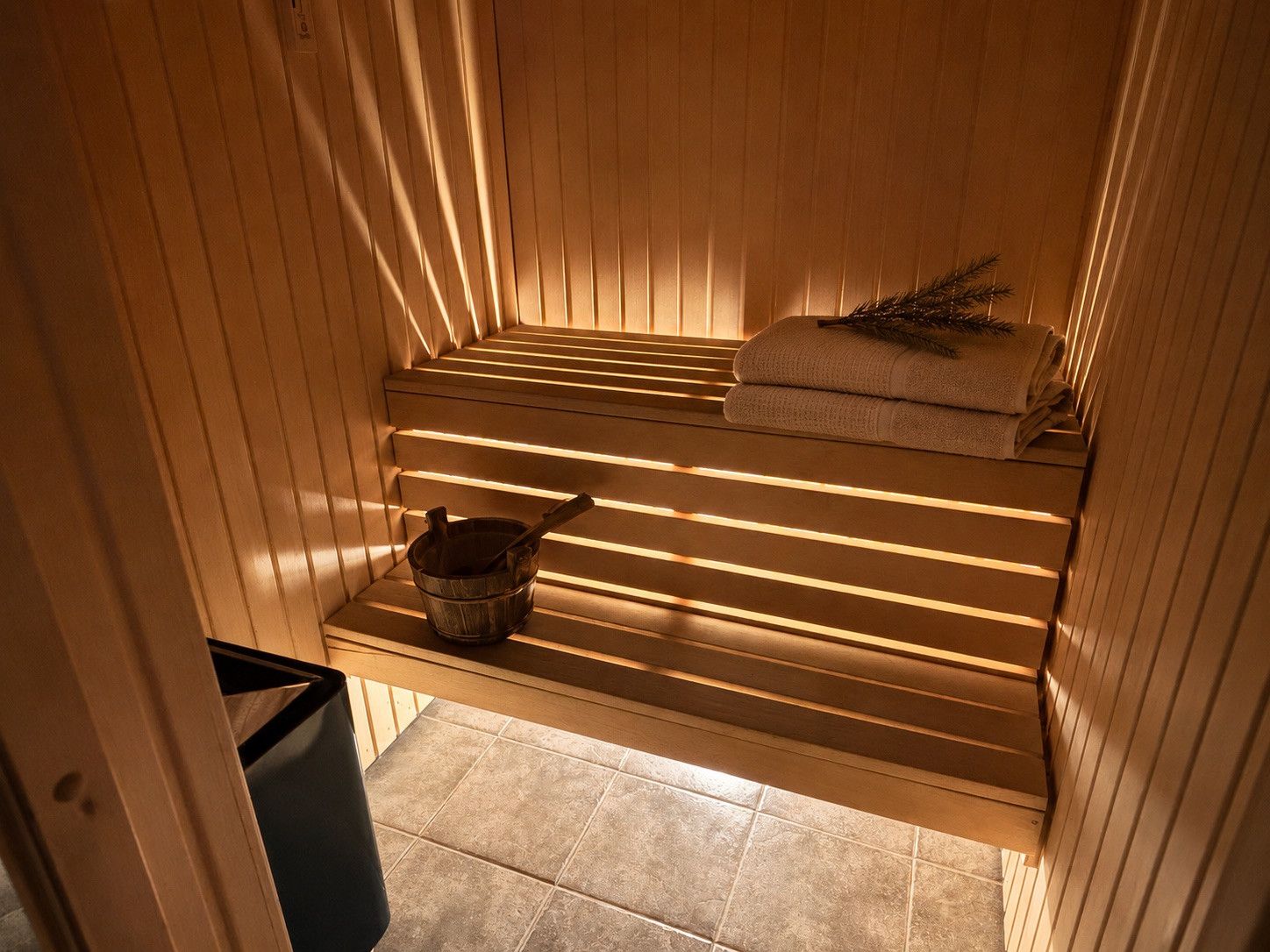 Un sauna avec des bancs en bois, un seau et des serviettes.