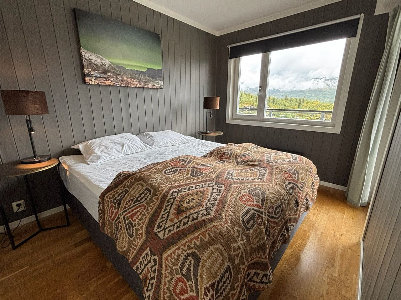Une chambre à coucher avec un lit, une fenêtre donnant sur un beau paysage, une lampe et un tableau accroché au mur.