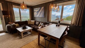 Amplia sala de estar con mesa de comedor de madera, sofás de cuero y un ventanal con vistas a la montaña.