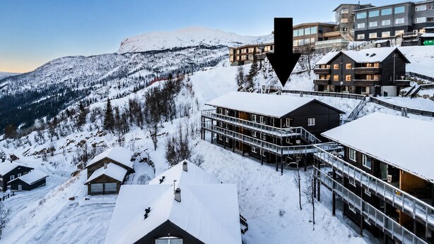Un complejo turístico nevado en la montaña con edificios modernos, un telesilla y un cielo despejado.