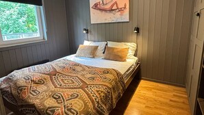 Un dormitorio con cama, colcha estampada, un cuadro en la pared y ventana con vistas a zonas verdes.