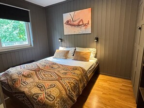 A bedroom with a bed, patterned bedspread, a painting on the wall, and a window with a view of greenery. - Mountain gem-  Ski in/out & panorama views (Hemsedal)