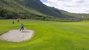 Campo de golf con un putting green, un búnker de arena y montañas al fondo.