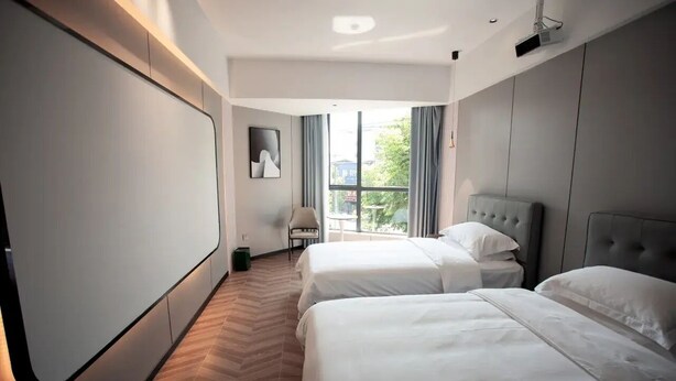 Habitación de hotel con dos camas, una silla, un ventanal grande y un proyector en el techo.