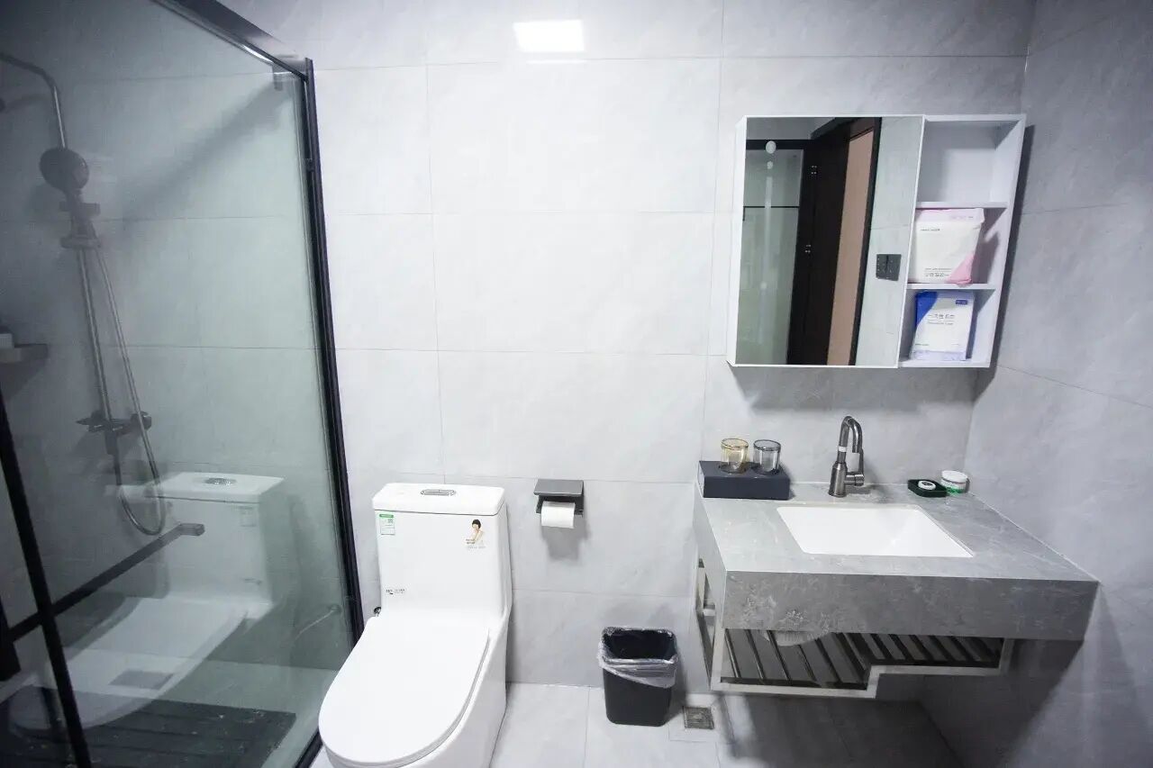 Un bagno moderno con doccia in vetro, un WC bianco, un lavandino con specchio e un cestino.