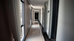 Un pasillo largo y estrecho con piso reflectante, grandes ventanales en un lado y puertas en el otro.