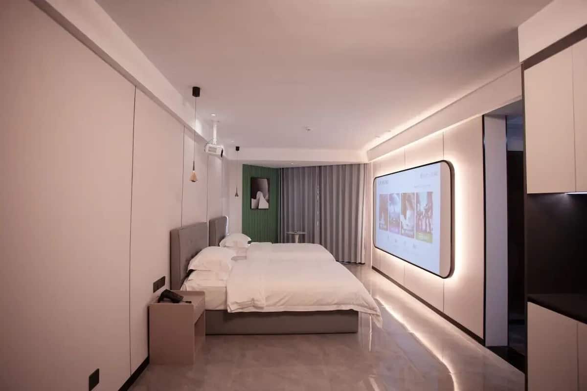 A modern hotel room with a large bed, a flat-screen TV, and a large window with curtains.