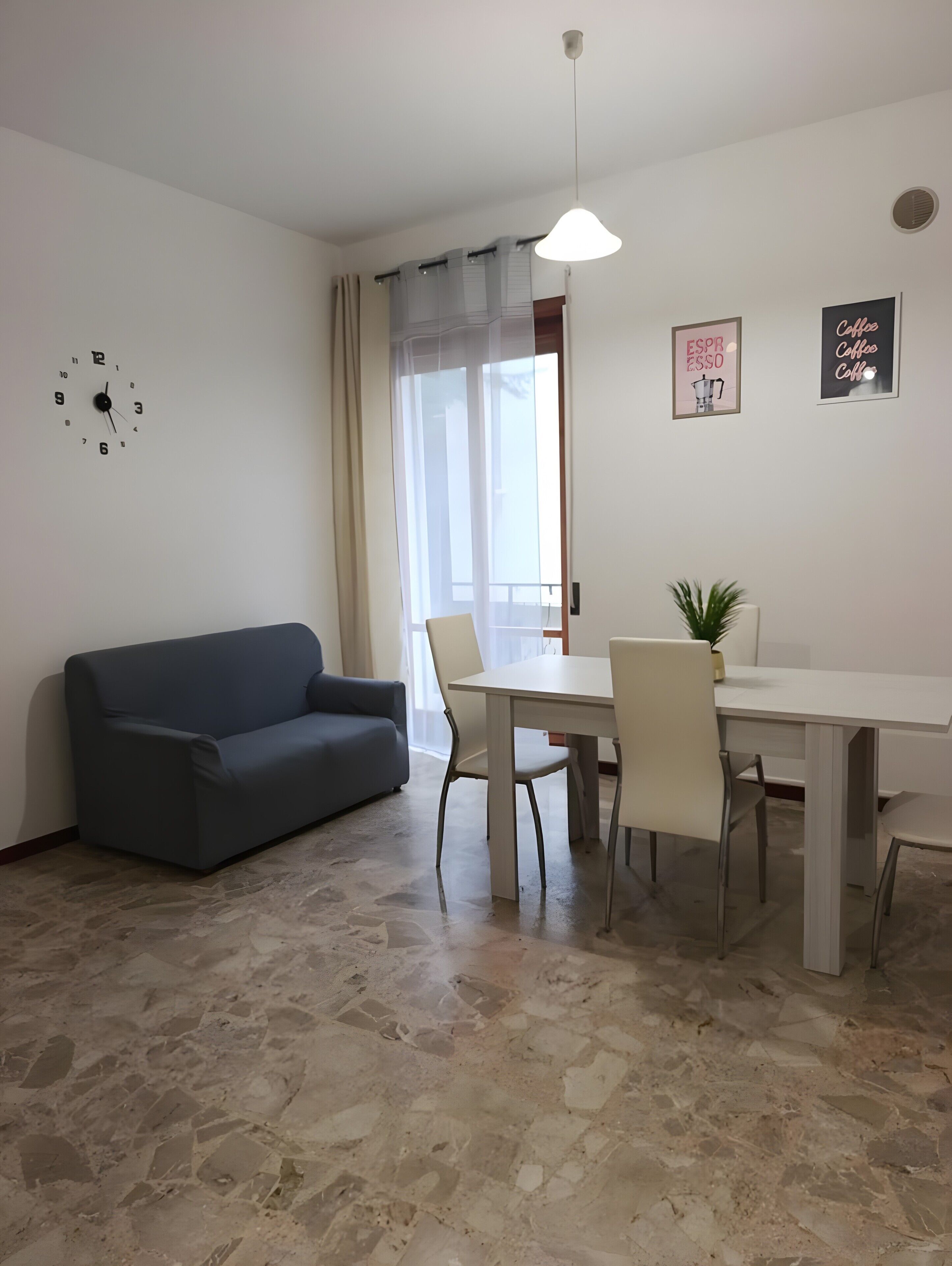 Ein Wohnzimmer mit einer Couch, einem Esstisch mit Stühlen, einer Uhr und zwei gerahmten Bildern an der Wand.