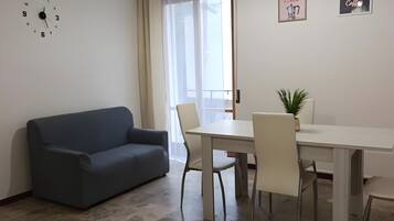 Ein Wohnzimmer mit einer Couch, einem Esstisch mit Stühlen, einer Uhr und zwei gerahmten Bildern an der Wand.