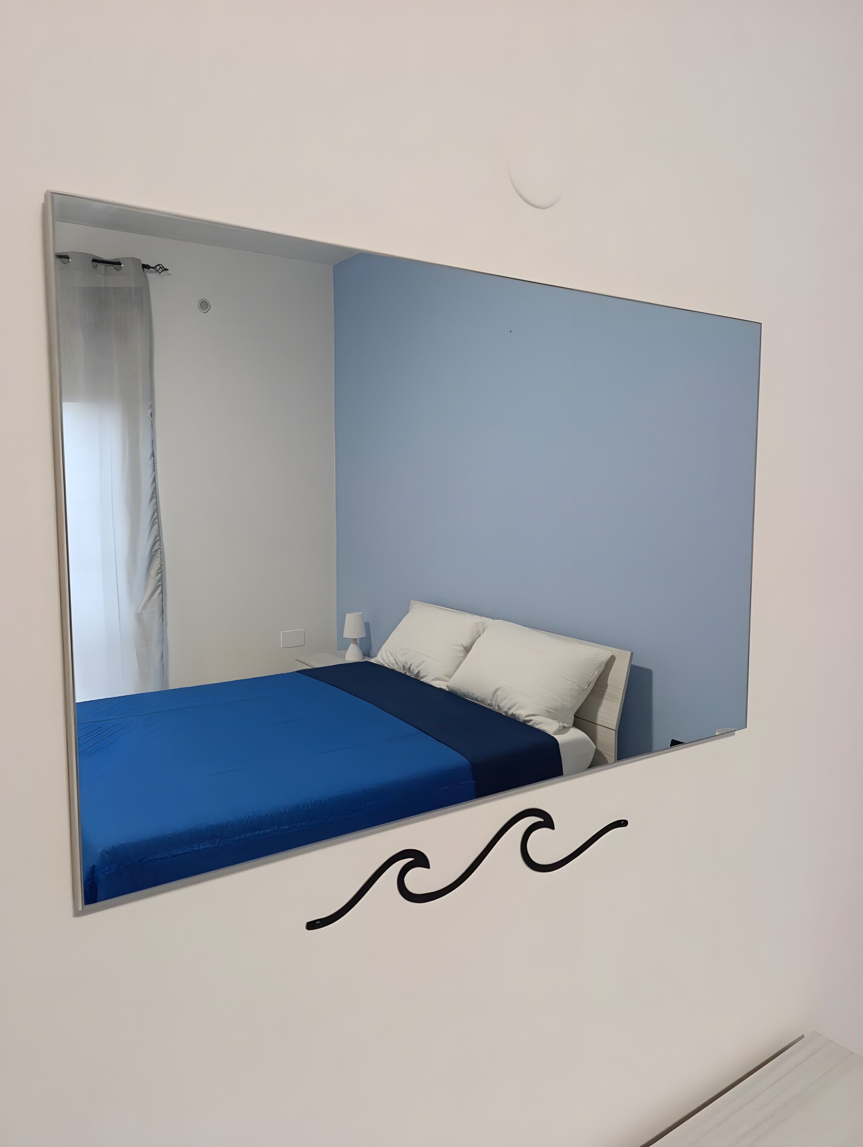Una habitación con cama, mesita de noche, lámpara y espejo.
