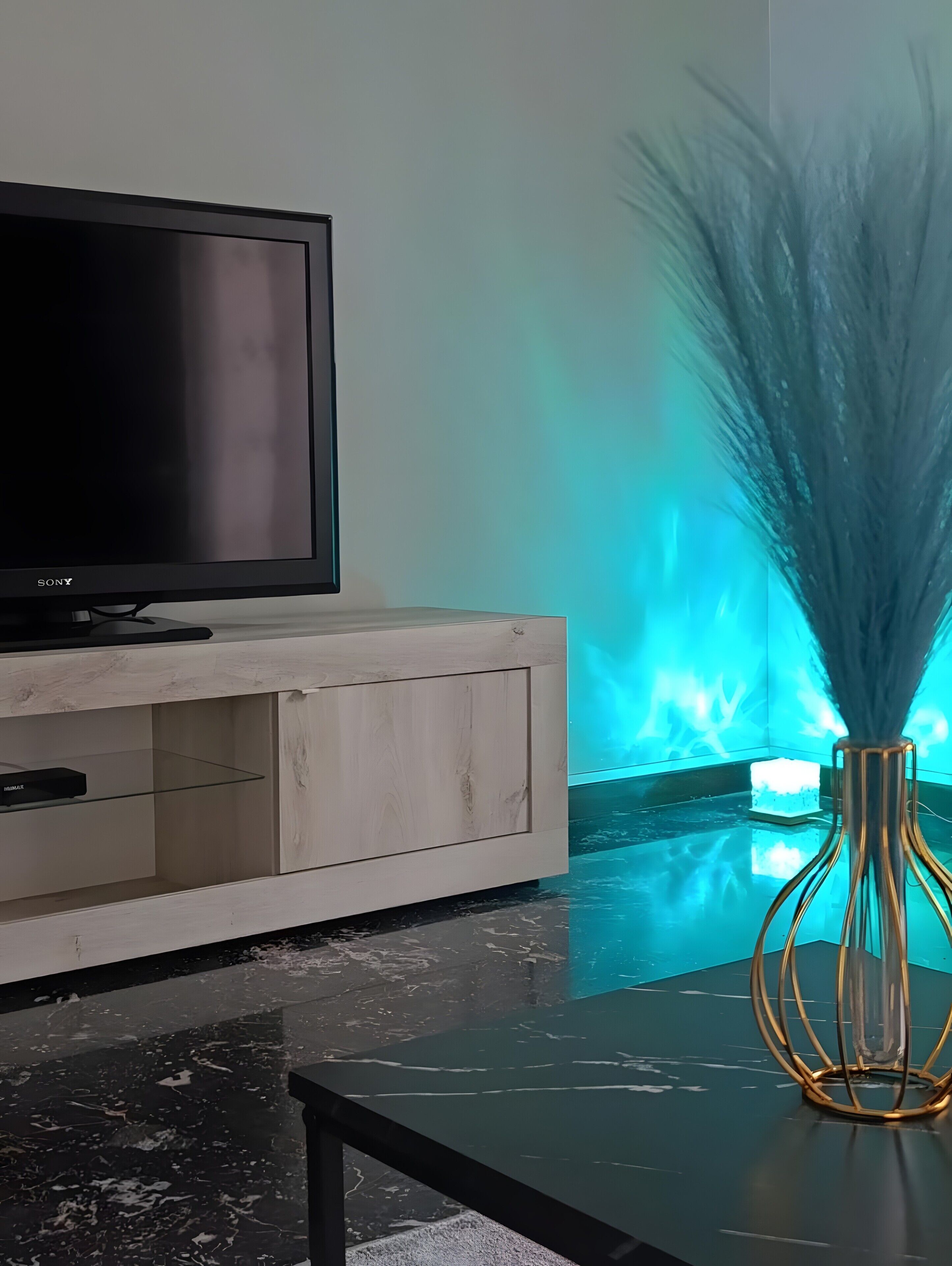 Ein modernes Wohnzimmer mit Flachbildfernseher auf einem Holzkabinett, einem Glastisch und einer dekorativen Vase mit hohen Gräsern.