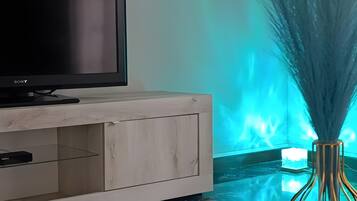 Ein modernes Wohnzimmer mit Flachbildfernseher auf einem Holzkabinett, einem Glastisch und einer dekorativen Vase mit hohen Gräsern.