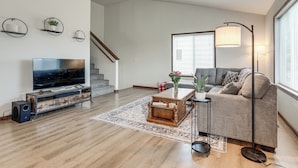 Een moderne woonkamer met een flatscreen televisie, een houten tv-meubel, een bank, een bijzettafeltje, een vloerlamp en een trap.