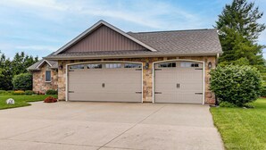 Une maison à deux étages avec une façade en pierre, deux portes de garage et une pelouse bien entretenue.