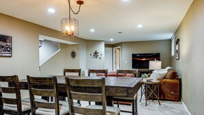 Un espace repas comprenant une table et des chaises en bois, un canapé, un téléviseur et un escalier.