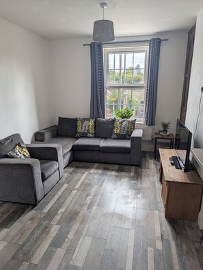 Una sala moderna con un sofá modular, una mesa de centro de madera y un televisor sobre un mueble.