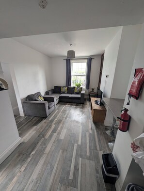 Un salón moderno con un sofá gris, suelo de madera y una ventana con cortinas.