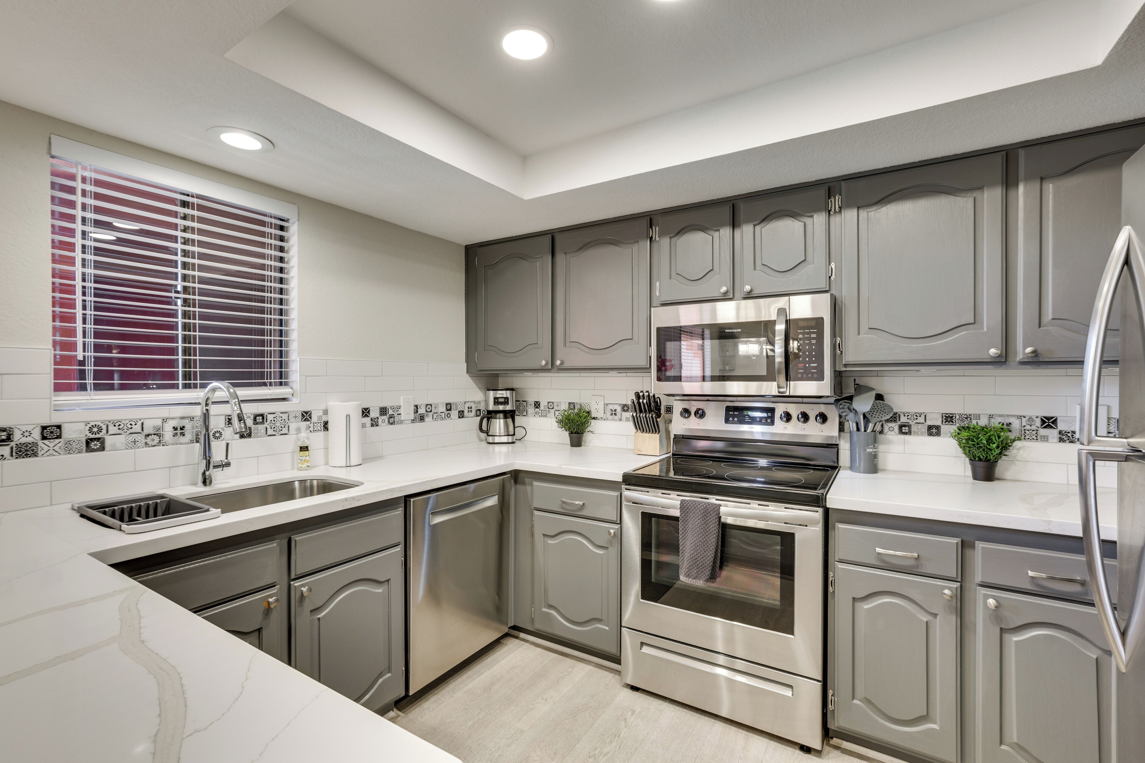A modern kitchen with grey cabinets, stainless steel appliances, a built-in oven, and a microwave.