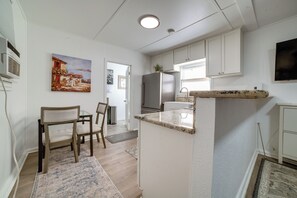 Eine Küche mit weißen Schränken, einem Kühlschrank, einem Essbereich mit Stühlen und einem Bild an der Wand.