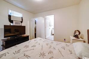 Ein Schlafzimmer mit einem Bett, einem Fernseher, einem Schminktisch, einem Spiegel und einer Tür zu einem anderen Raum.