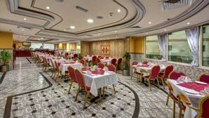 A banquet hall with marble flooring, red and gold chairs, white tablecloths, and a large decorative wall.
