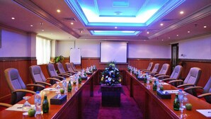 A conference room with a long table, chairs, a projector screen, and floral centerpieces.