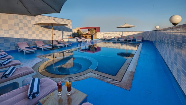 A rooftop infinity pool with lounge chairs and umbrellas, a bar area, and a tiled wall.