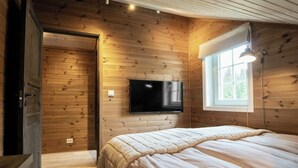 A wooden-paneled room with a bed, a TV mounted on the wall, and a window with a lamp. - Cabin in Uvdal with ski trails on the doorstep (UVDAL)