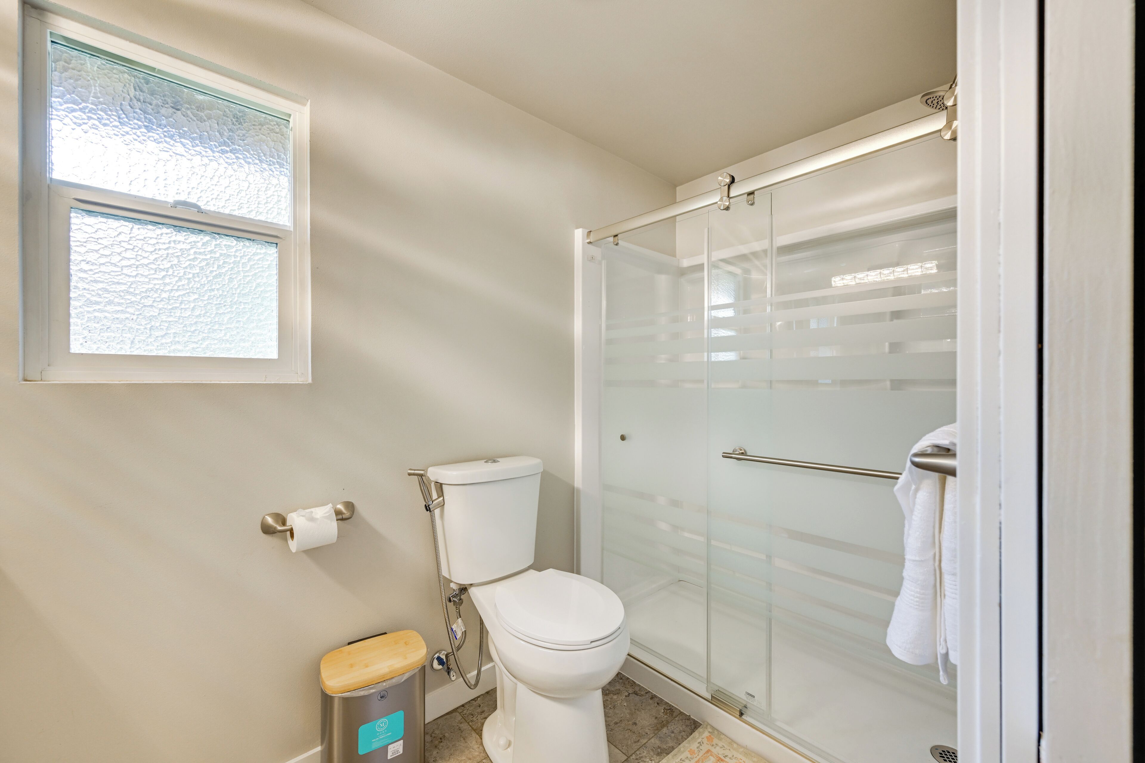 Ein Badezimmer mit Toilette, einer Duschkabine aus Glas, einem Fenster und einem Handtuchhalter.