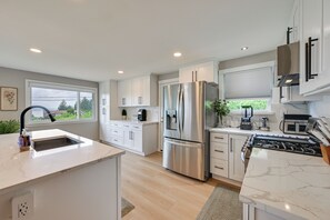 A modern kitchen with white cabinetry, stainless steel appliances, and a large window. - Quiet Home w/ Deck & Water Views in Des Moines (Des Moines)