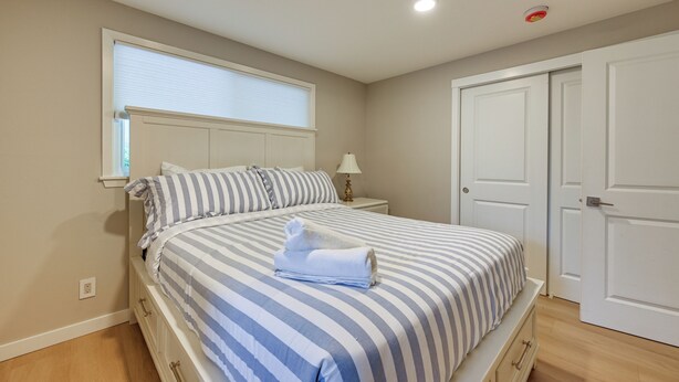 Een slaapkamer met een bed, nachtkastje, lamp, raam met jaloezieën en een deur.