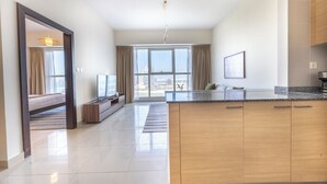 A modern kitchen with a large island, a dining area with a sofa, and a view of the city through large windows. - Bloomfields 1BR in Marina Bay 1  (Abu Dhabi)
