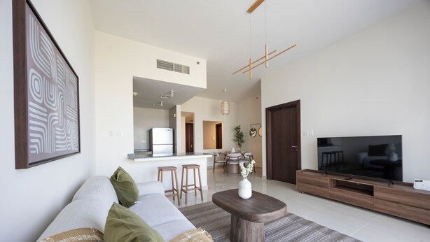 A modern living room with a sofa, coffee table, TV, and a kitchen area in the background. - Bloomfields 1BR in Marina Bay 1  (Abu Dhabi)